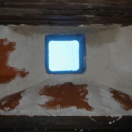 Hotte de cheminée vue d'en-dessous, chapeautée d'un boisseau de cheminée en terre cuite.